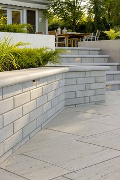 a white brick wall next to a patio with plants growing on the ledge and steps