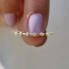 a woman's hand holding a gold ring with five small white stones on it