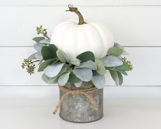 a white pumpkin sitting on top of a metal container filled with leaves and greenery