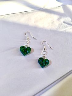 green heart shaped earrings sitting on top of a white sheet with silver earwires