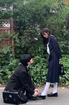 a man and woman standing next to each other in front of bushes with trees behind them