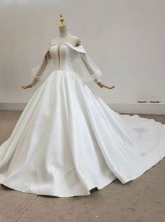 a white wedding dress with long sleeves and a train on display in a room full of mannequins