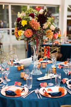 a blue table cloth topped with plates and vases filled with orange and yellow flowers