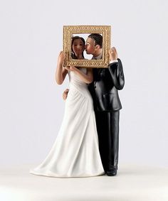 a wedding cake topper with a bride and groom holding up a gold framed photo