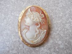 Welcome! Beautiful Shell cameo brooch pin, marked 10 k gold on the back, with fine carved hair and she has a tiara in her hair. The cameo is in excellent condition and the clasp in the back is a c clamp and there is a loop in the top of the back to have the piece to be used as a necklace. It was made in Italy probably in the Naples area. It measures less than an inch and 3/4 by 1 1/2 inches. The clasp is perfect working condition. Thanks for looking! Classic Gold Brooch With Intaglio Detail, Classic Gold Intaglio Brooch, Classic Gold Intaglio Brooches, Classic Gold Brooches With Intaglio, Ornate Oval Carved Brooches, Ornate Carved Oval Brooches, Ornate Carved Collectible Brooches, Antique Gold Intaglio Brooches, Ornate Carved Gold Brooches