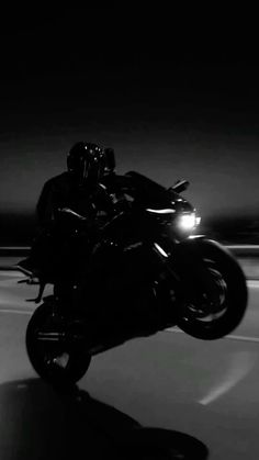 black and white photograph of a person riding a motorcycle in the dark with headlights on