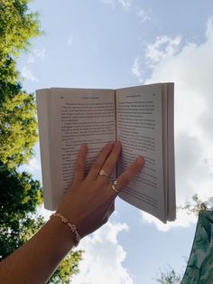 a person is holding an open book in their hand and looking up into the sky