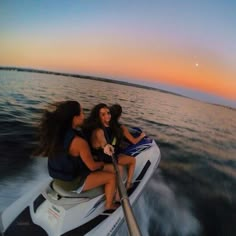 three girls are riding on the back of a boat at sunset in the water with their backs turned to the camera