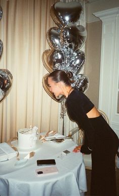 a woman standing in front of a table with silver balloons on the wall behind her