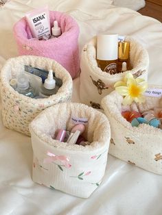 three small storage baskets sitting on top of a white bed covered in blankets and personal care items