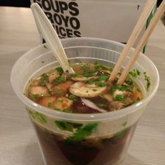 a plastic cup filled with soup and chopsticks