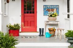 a red door sits in front of a white house with potted plants on the porch