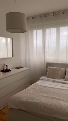 a white bed sitting under a window next to a dresser and mirror in a bedroom