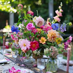 a table set with plates and vases filled with flowers, candles and napkins