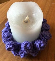 a white candle sitting on top of a wooden table next to a purple crocheted ring