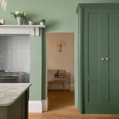 a kitchen with green cabinets and marble counter tops, along with an open door leading to the dining room