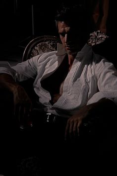 a man sitting in the dark with his shirt open