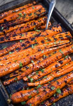 grilled carrots in a pan with a fork on the side and garnished with parsley