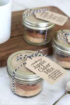 three mason jars with labels on them sitting on a counter next to a spoon and cup