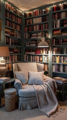 a living room filled with lots of bookshelves covered in blankets and pillows next to a lamp