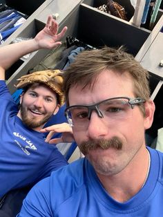 two men in blue shirts are posing for the camera with their hands up and one is wearing glasses