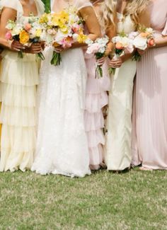 a group of women standing next to each other holding bouquets in their hands and wearing long dresses