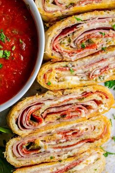 several sandwiches with meat and tomato sauce on the side next to a bowl of soup