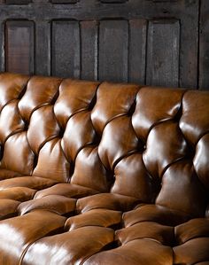 a brown leather couch sitting in front of a wooden wall