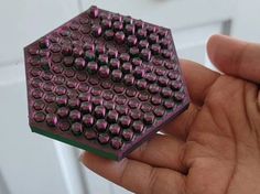 a close up of a person's hand holding a small piece of purple metal