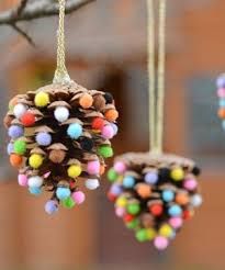 pine cone ornaments with colored pom - poms hanging from strings