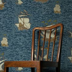 a wooden chair sitting in front of a blue wallpaper with ships on the ocean