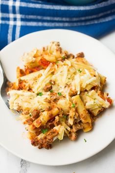 a white plate topped with pasta and meat covered in sauce next to a blue dish towel