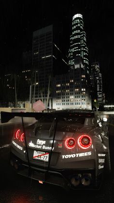 the back end of a car with its lights on in front of a cityscape