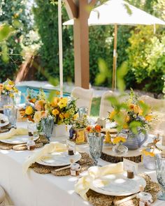 an outdoor table set with plates and flowers