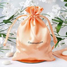 an orange satin bag sitting on top of a table next to white flowers and candles