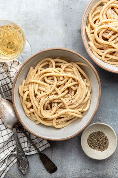 two bowls filled with pasta next to a glass of wine