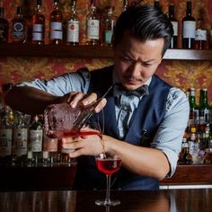 a man pouring a drink into a glass at a bar with liquor bottles in the background