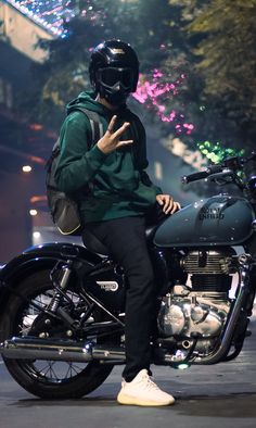 a man sitting on top of a motorcycle giving the peace sign with his hand while wearing a helmet