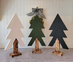 three wooden christmas trees sitting on top of a striped tablecloth covered floor next to a wall