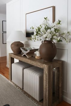 a vase with white flowers on top of a wooden table next to a mirror and lamp