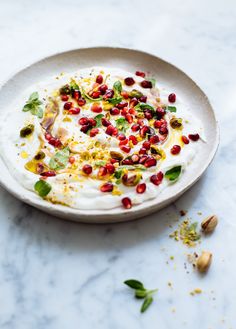 a white plate topped with food on top of a marble counter next to nuts and herbs