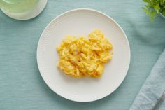 a white plate topped with scrambled eggs on top of a blue table cloth next to a fork and knife