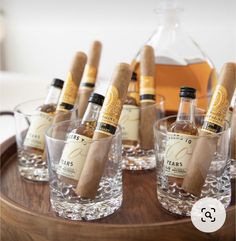 several bottles and glasses with cigars in them on a wooden tray next to a bottle