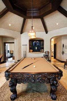 a pool table in the middle of a living room with stairs and chandelier