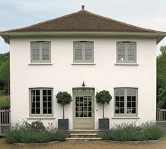 a large white house with three windows and two bushes in front of the entrance to it