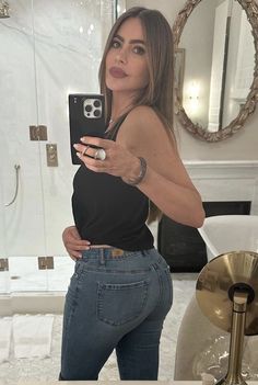 a woman taking a selfie in front of a mirror with her cell phone up to her waist