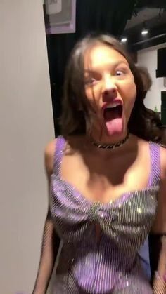 a woman with her mouth open and tongue out in front of the camera while wearing a purple dress