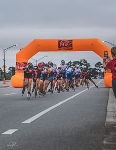 a group of people riding skateboards down a street under an orange arch overpass