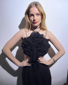 a woman standing in front of a white wall with her hands on her hips wearing a black dress