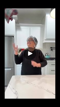 an older woman standing in front of a kitchen counter with her hands out to the side